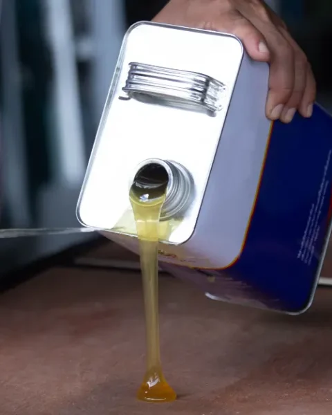 Worker pouring thick rubber-based adhesive from a metal container onto a surface for industrial bonding.